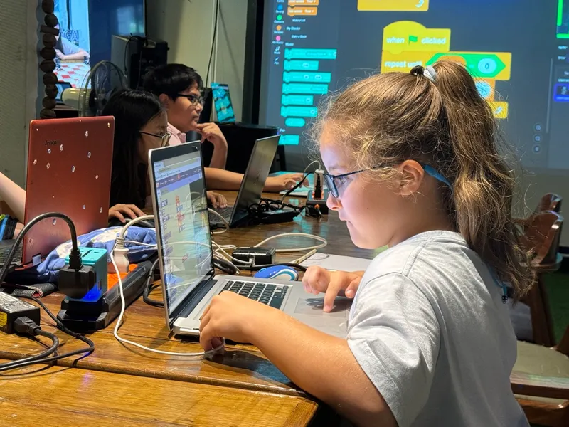Girl with glasses leaning forward and actively coding at Little Geek Academy