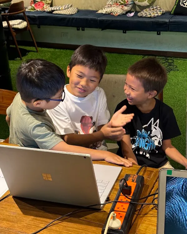 Three kids laughing and collaborating on a coding project together